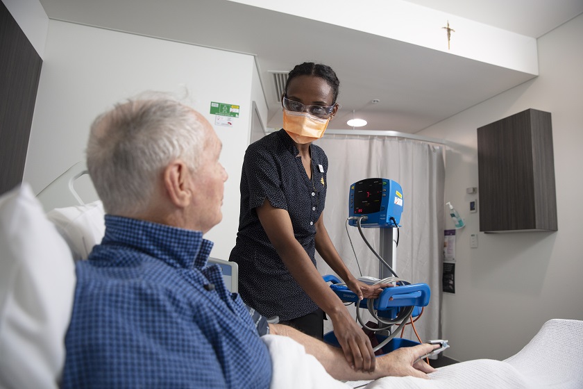 A nurse checks a patient's pulse in a hospital room.