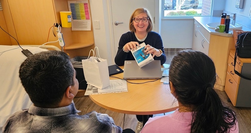 Caregiver facing two patients in a consultation room holding a blood glucose monitor and smiling