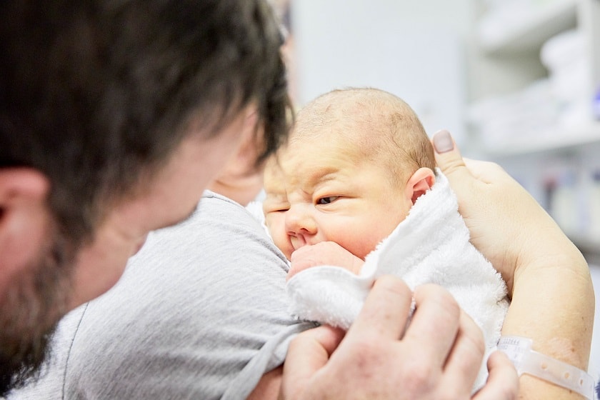 Mother holding infant in their arms as father smiles at baby