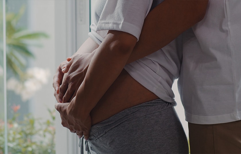 Pregnant couple by window cradling belly