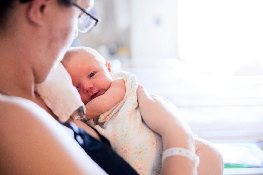 Mother wearing hospital bracelet looking at newborn she's holding in her arms