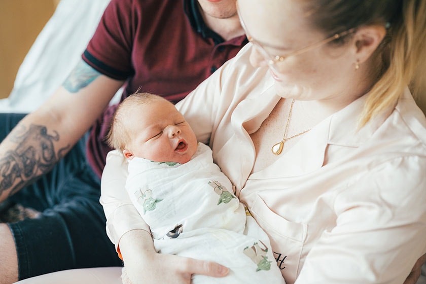 A mother cradles her yawning newborn while the father sits next to her watching on.