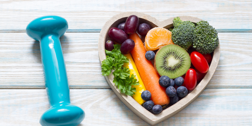 Image of blue dumbbell next to plate of fresh fruit and vegetables in the shape of a love heart 