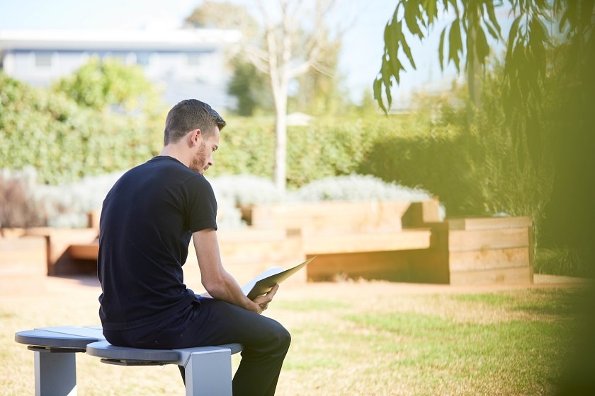 Young adult sits on bench seat outdoors while reading