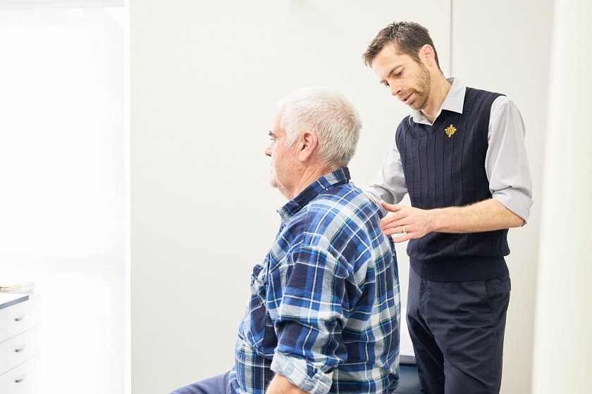 Patient sitting upright with allied health worker inspecting their back