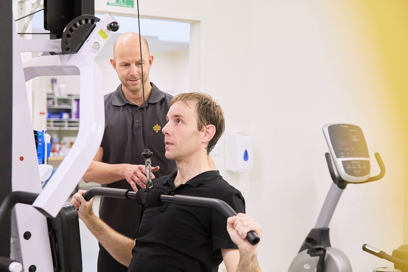 Allied health worker standing instructing seated patient using rehabilitation equipment