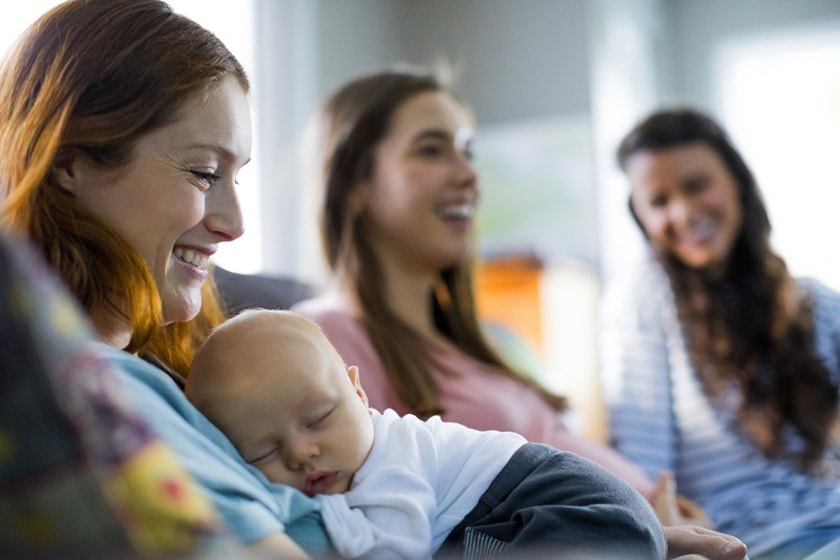Three people smiling as a baby sleeps on one of their chests.