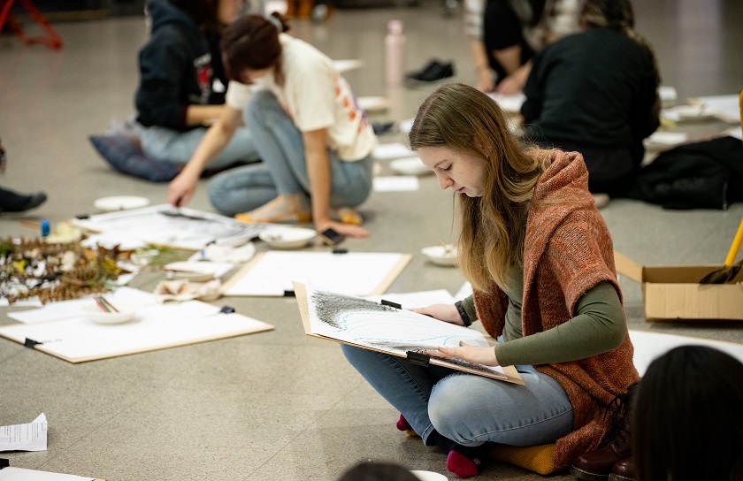 A person sitting, making art on a piece of paper.