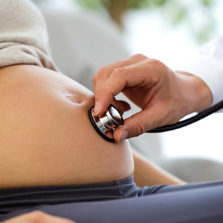 Close up of pregnant patient seated with stethoscope on abdomen