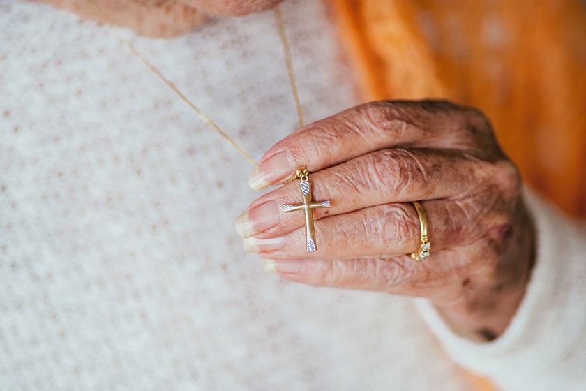 An elderly hand holds on to the crucifix pendant of a necklace