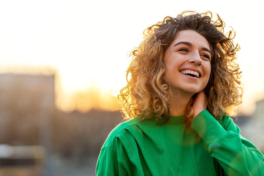 A young woman smiles against the backdrop of a sunset.