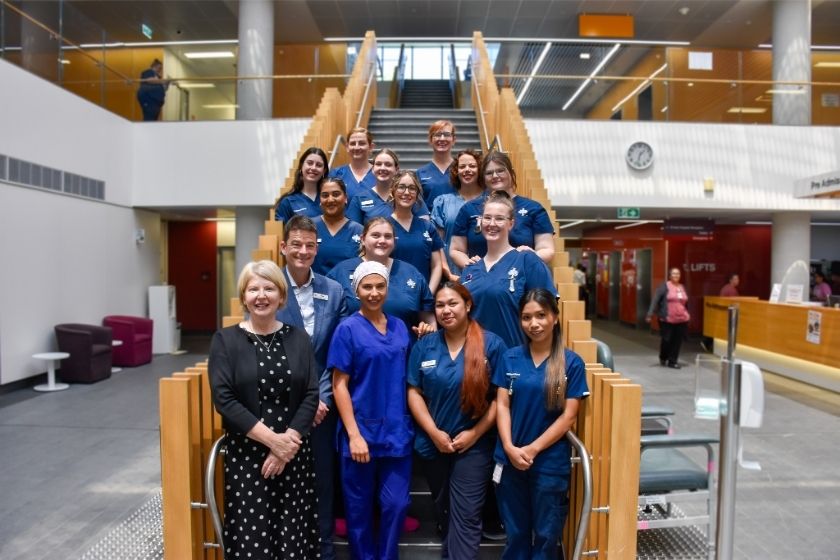 Caregivers standing on a staircase in a hospital, smiling at the camera.