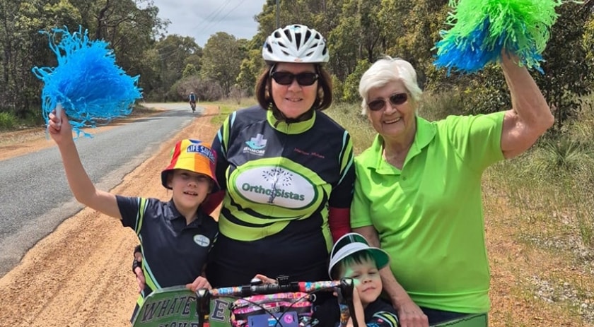 A member of the ortho sistas posing on her bike, flanked by supporters with signs