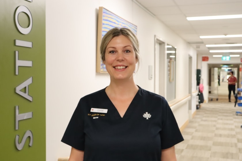 A woman in a blue scrub standing in a hallway in a medical setting