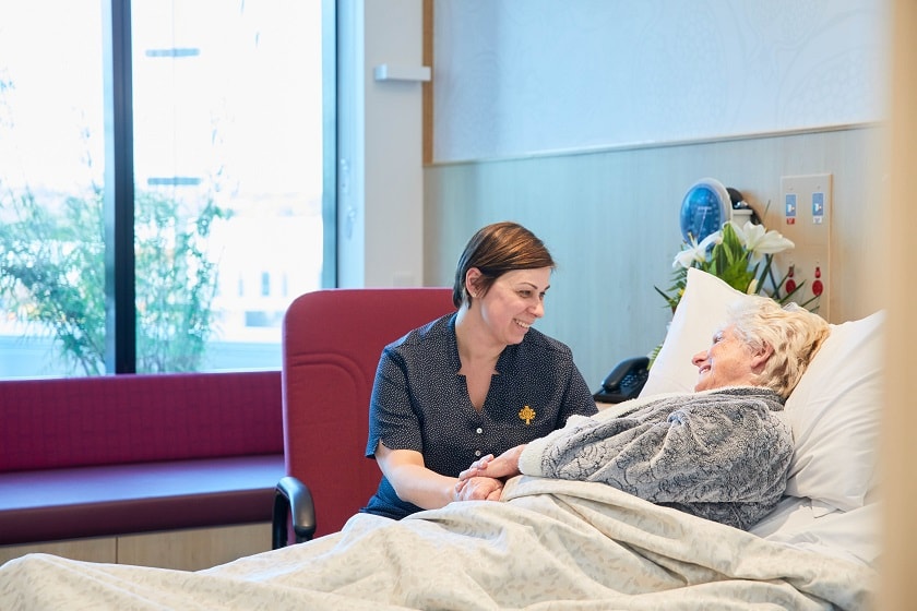 St John of God Health Care caregiver sitting by the bedside of a patient