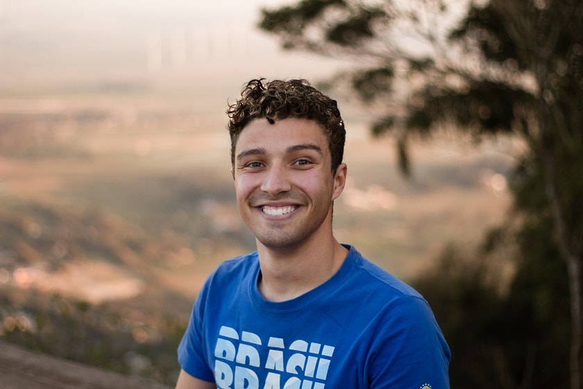 A person smiling at the camera with an out of focus view of a valley behind him.