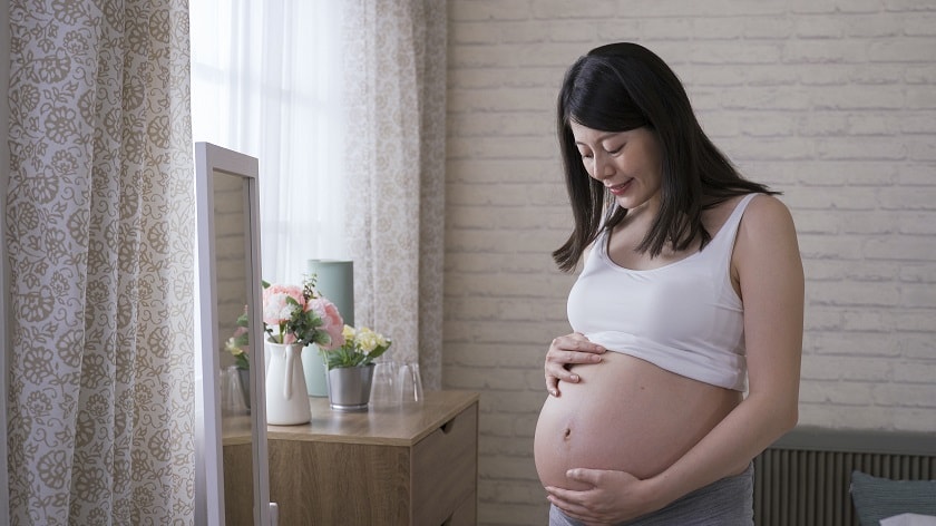 A pregnant woman holding her abdomen in front of a mirror.