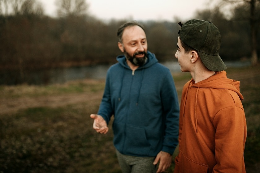 A man and young man walking in a park talking to each other.