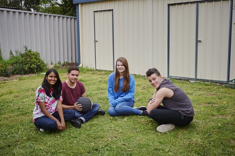 Four young adults sitting on the grass in a back yard.