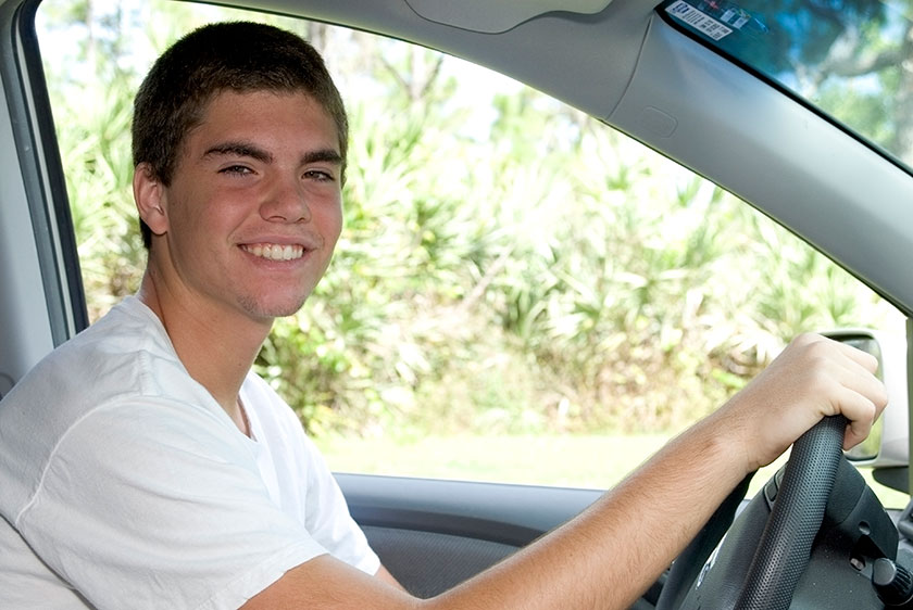 A person of youth sitting in the drivers seat of a car and smiling