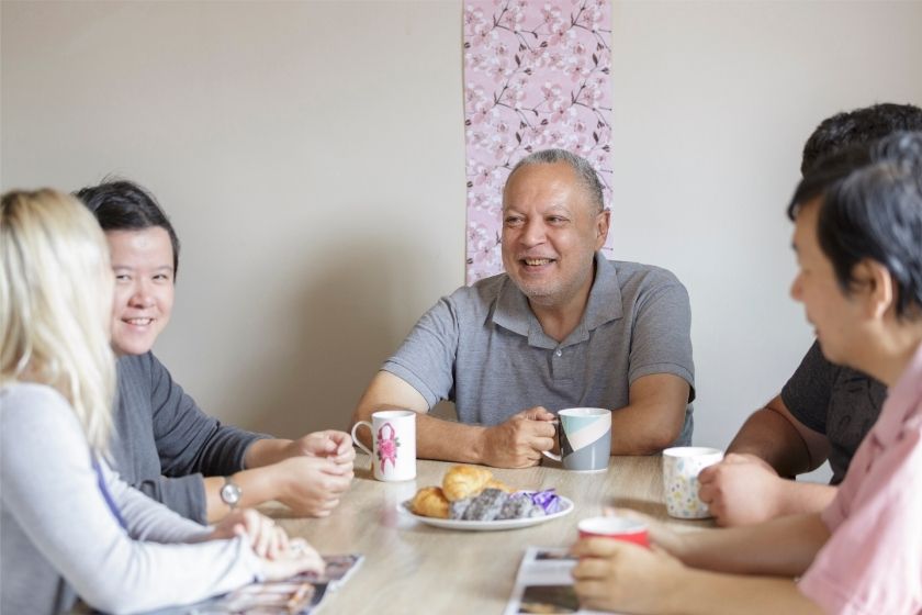 People sitting around a table with mugs in their hands and a plate of snacks on a plate in the middle.
