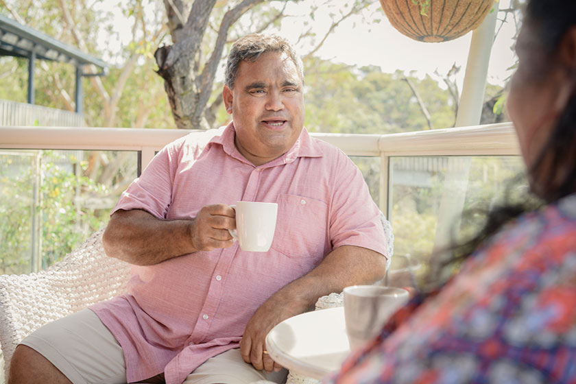 Person sitting on outdoor balcony setting facing another person whilst drinking from a mug