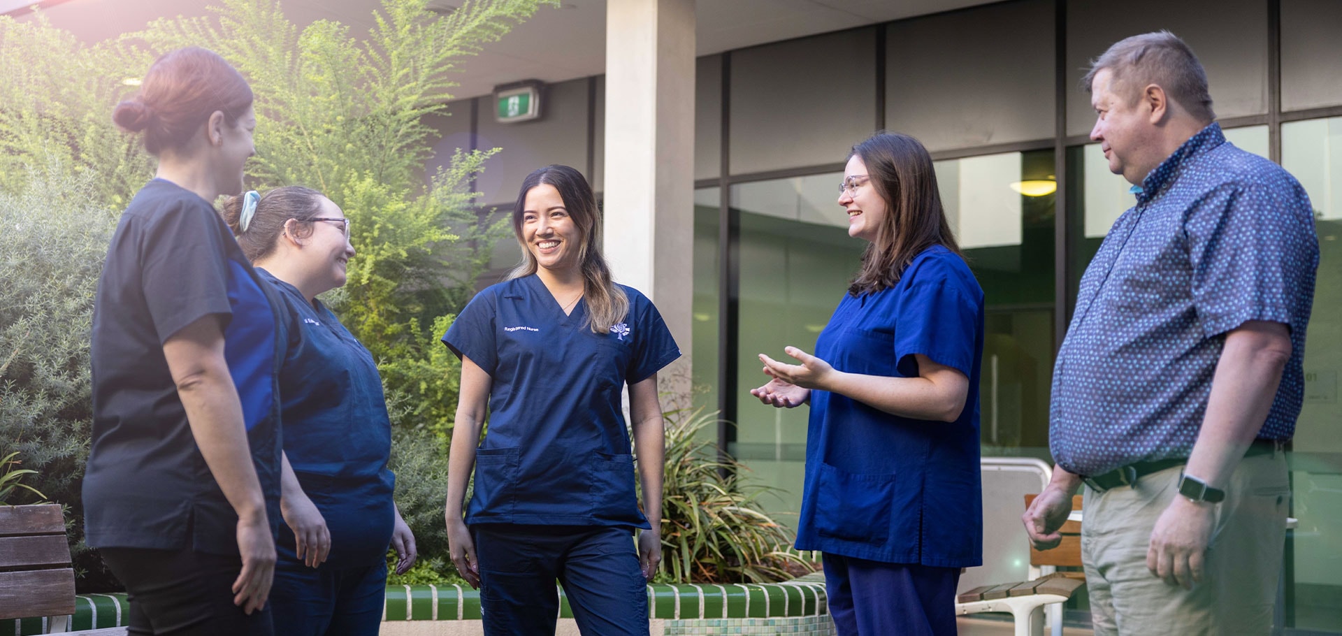 Candid image of a group of caregivers with some dressed in scrubs and others in business wear, standing outside conversing and smiling.