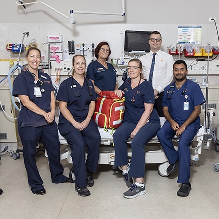 Caregivers dressed in dark blue scrubs surround a bed inside the Emergency Department at St John of God Murdoch Hospital