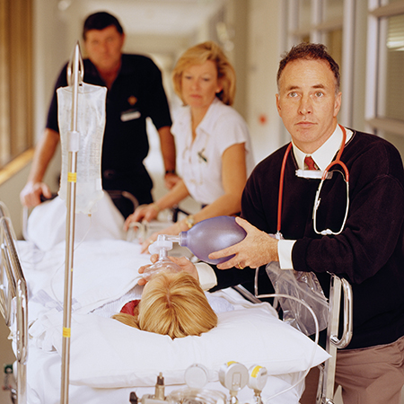 Caregivers assist a patient lying in a bed while walking down a corridor inside the Emergency Department