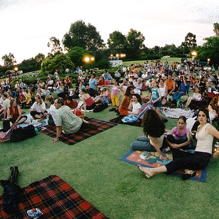 Large crowd seated on picnic blankets on the grass at the community carols by candlelight event