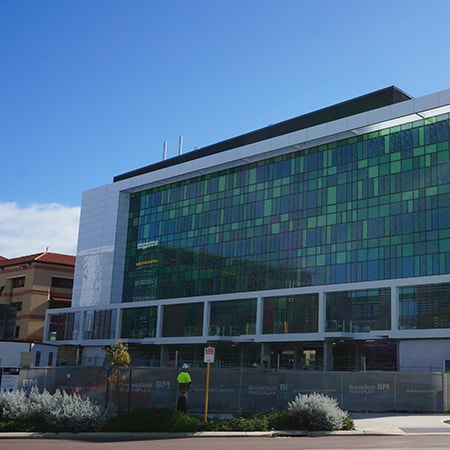 Exterior of St John of God Murdoch Hospital South Wing surrounded by scaffold fencing with construction workers in foreground