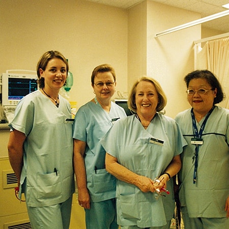 Four caregivers dressed in light blue scrubs smile at the camera in the main theatre suite