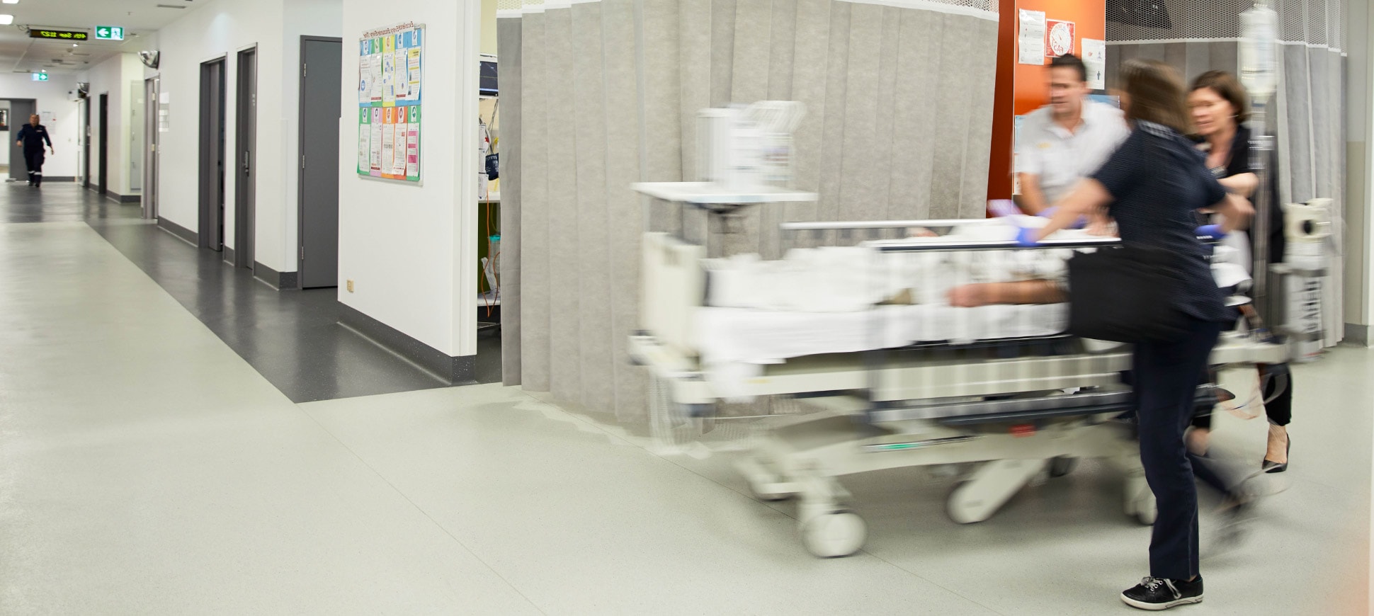 Three caregivers push a patient in a hospital bed around the corner