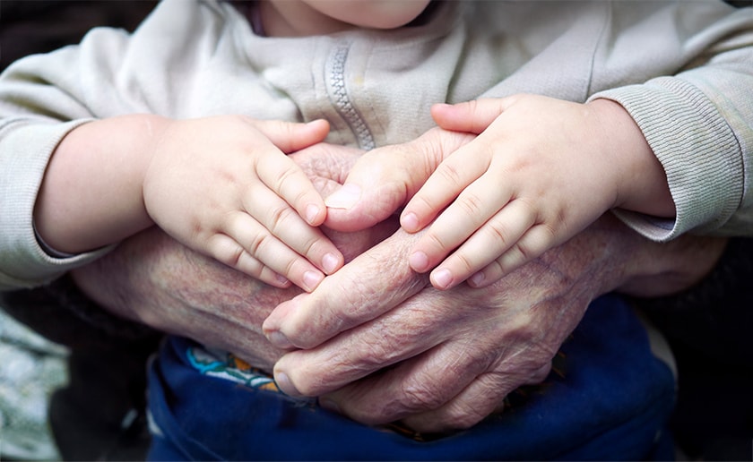 A pair of small children's hands rests over a pair of old hands
