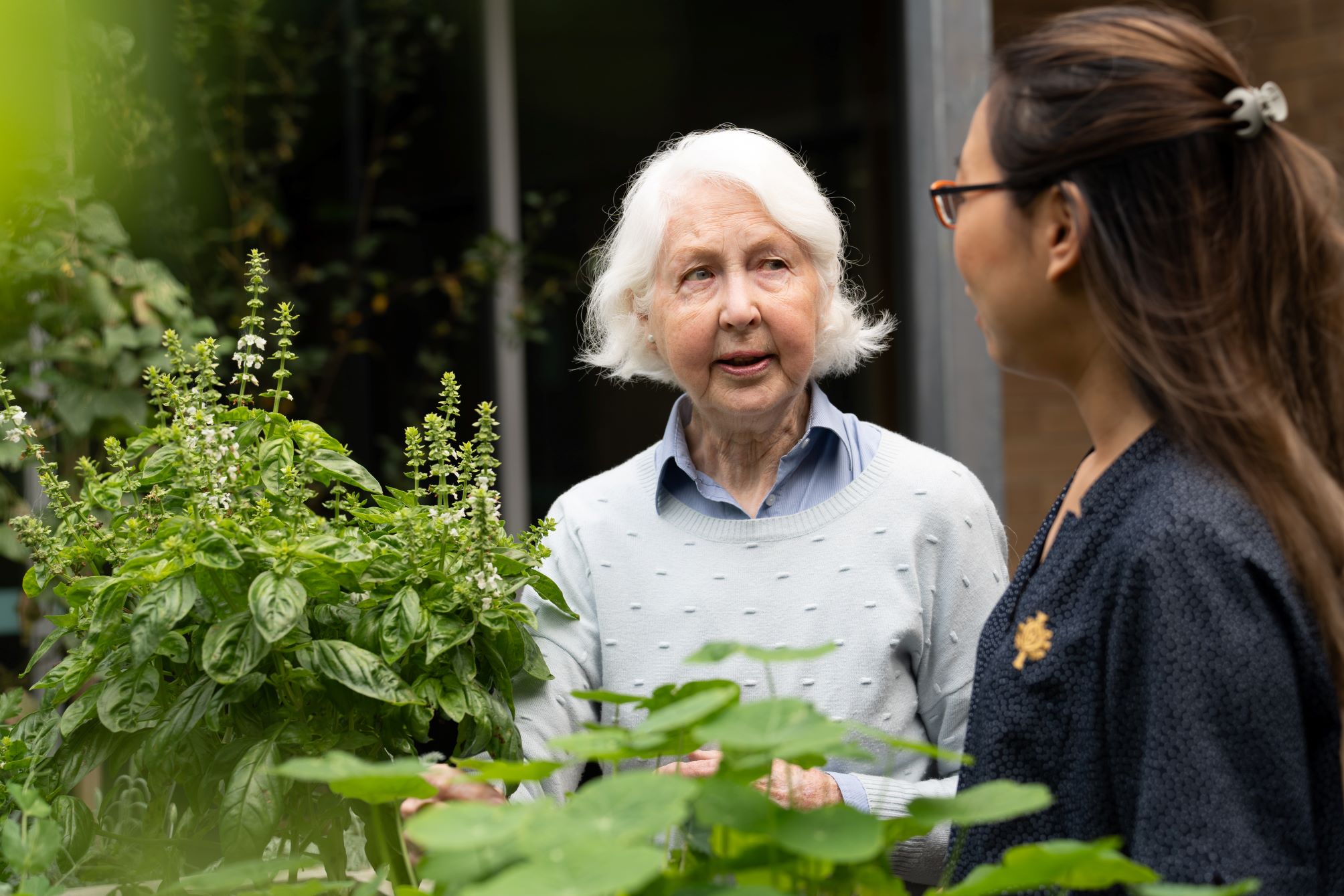 Caregiver and elderly patient talking outside in garden