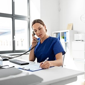 A doctor talks on the phone in a clinical office while writing notes on a form