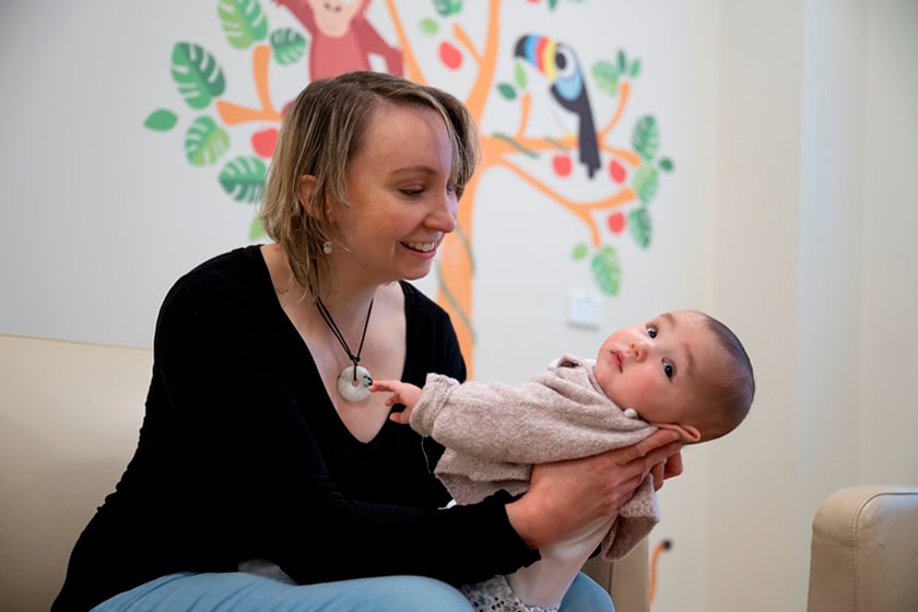 Person cradling baby in both hands whilst sitting on a couch looking at baby.