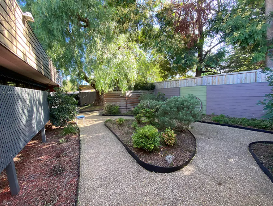 A serene looking garden with walking paths and native plants, surrounded by big trees