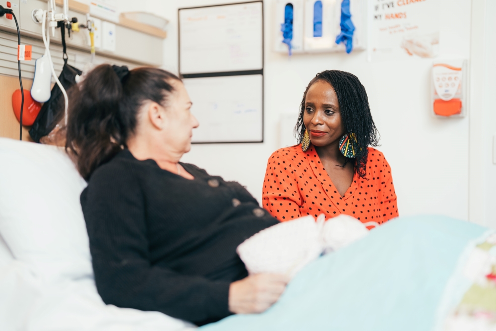 Pastoral care worker sitting beside patient in bed