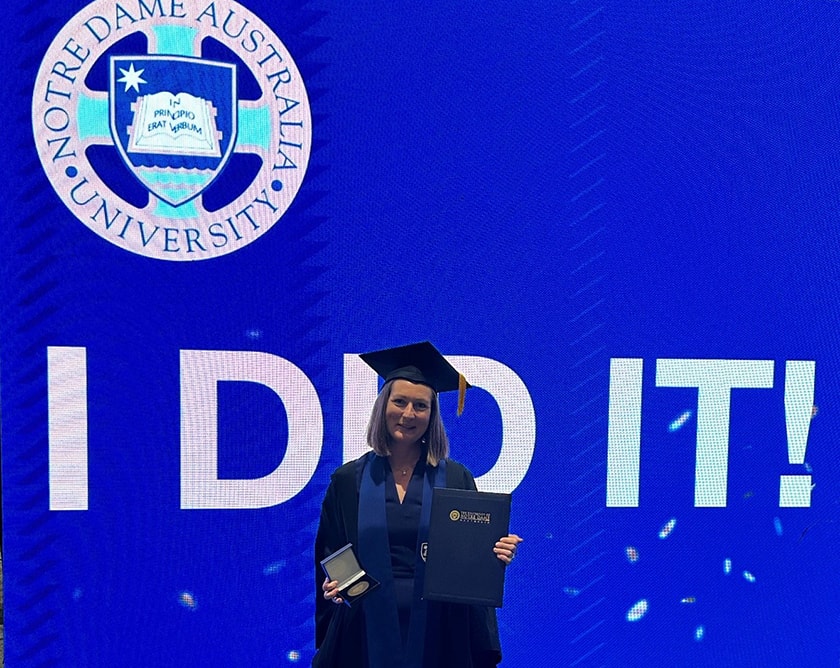Image of RN graduate Meesha Astill standing in front of Notre Dame poster