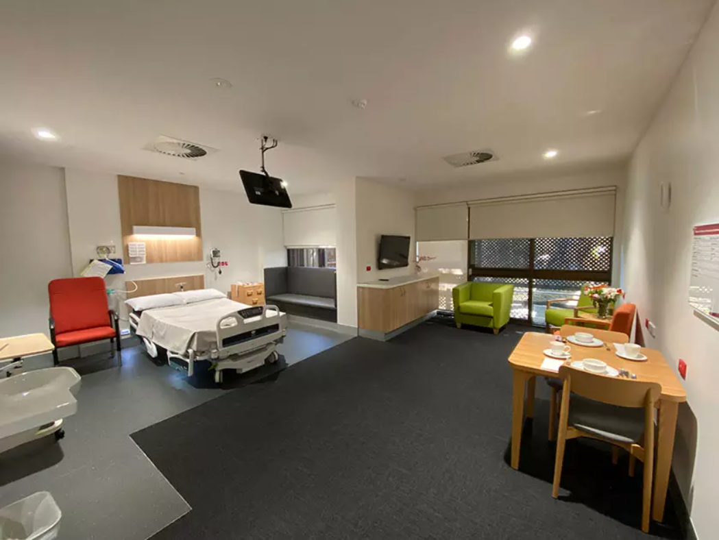 A luxurious looking hospital room with a big bed, dining table, couch and tv's