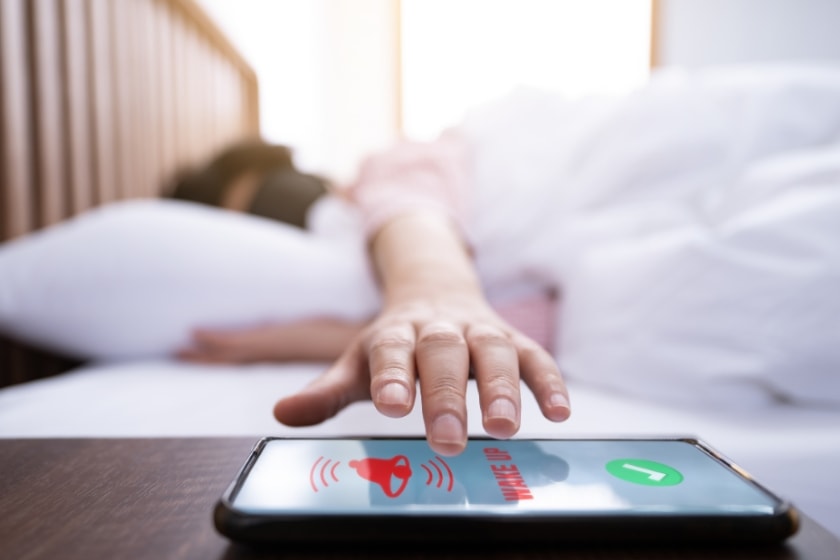 a hand reaching out to a phone with the phone's alarm going off