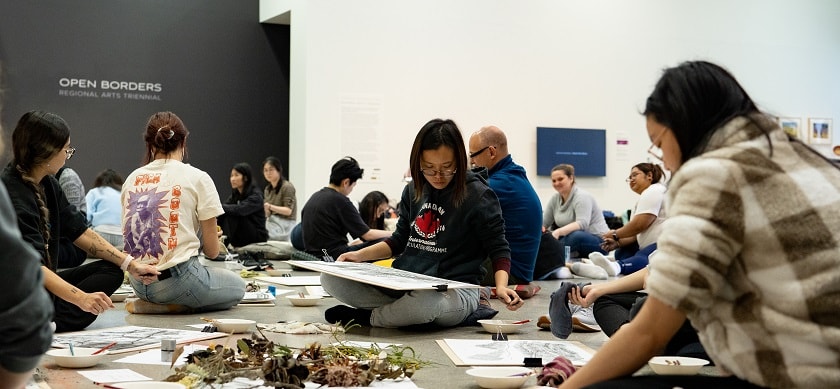 People sitting on the floor making art on pieces of paper.