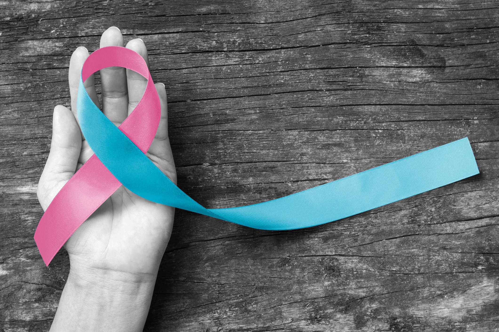 A hand holding a pink and blue ribbon