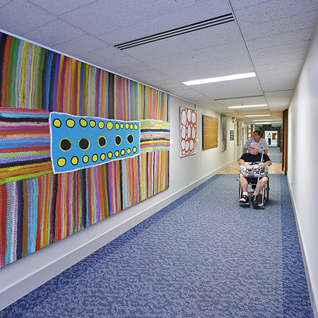 patient in wheelchair getting moved through corridor with artwork 