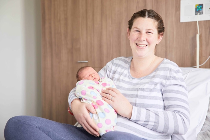 Mother sitting on bed holding newborn