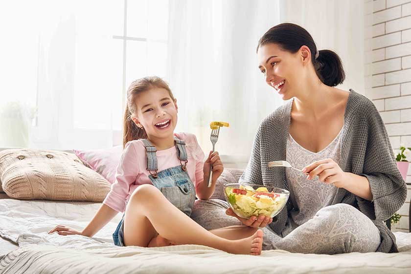 A woman and girl eating fruit from a bowl