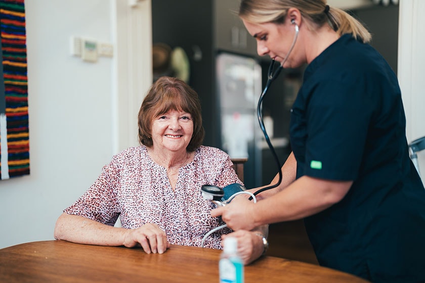 Healthcare at Home hospital care patient seated at table having blood pressure taken by caregiver