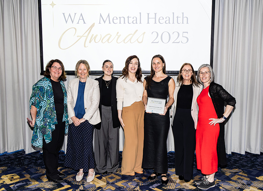 The St John of God Raphael Services team smiles in front of an event screen that reads 'WA Mental Health Awards 2025'