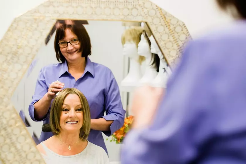 A patient looks in a mirror after help with choosing a wig